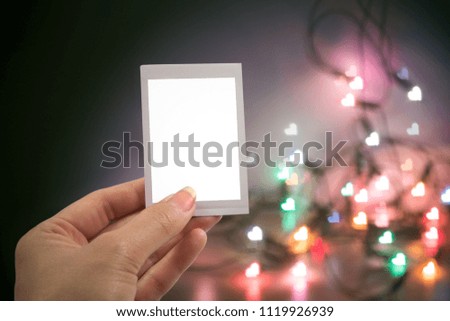 Hand holding instant photo or picture frame with blurred christmas lights background with copy space warm retro vintage tone.