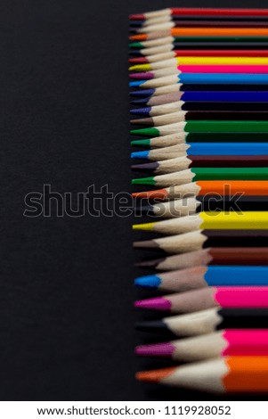 Colored pencils lined in a row on a black background background.