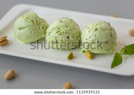 Tasty pistachio ice cream with nuts, decorated with mint leaves, light background. 