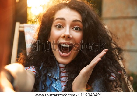 Image of shocked surprised young beautiful curly woman outdoors in park looking at camera.