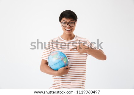Picture of smart asian student man wearing striped t-shirt and eyeglasses holding and pointing finger at globe during lesson isolated over white background