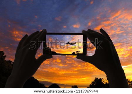 A woman take a picture of the airplane on the sunset sky  on mobile phone