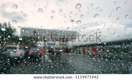 Visibility is limited when driving through a rain storm, raindrops splatter on the windshield. View through car window blurry with heavy rain. 
