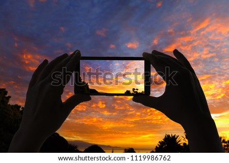 A female's hands take a picture of silhouette of palm trees and Atlantic sea on La Gomera island on mobile phone. Canary Islands at sunset