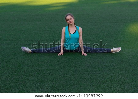 Sporty beautiful girl with two pigtails sitting on a twine on the green grass at the stadium in the summer