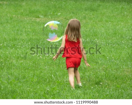 A little girl playing on a green meadow with a soap bubble. Happy childhood, summer leisure, children's outdoor games, running joyful child