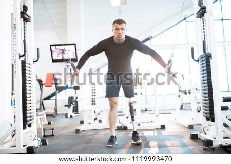 Full length of handsome man with prosthetic leg working out with machines in modern sunlit gym, copy space