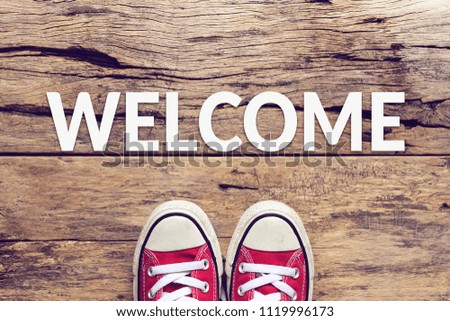 welcome sign text on wooden floor with red sneaker on it