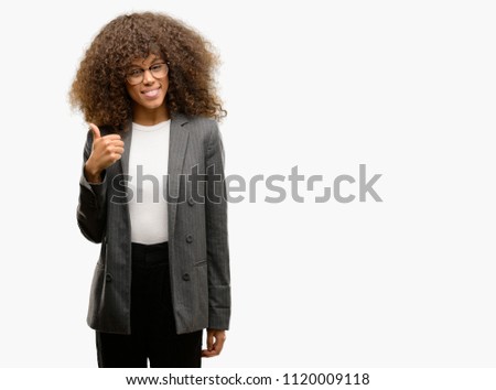 African american business woman wearing glasses doing happy thumbs up gesture with hand. Approving expression looking at the camera with showing success.