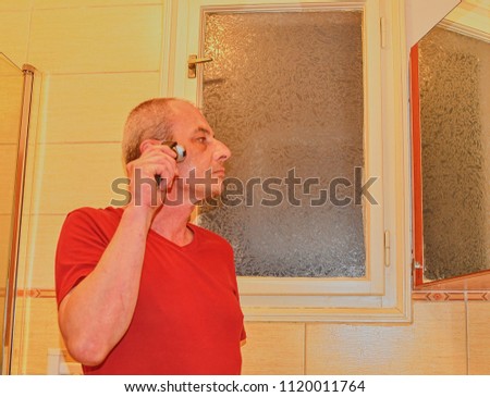 Middle aged man shaving in a bathroom, using electric razor. Mature man at home. Senior concept. 