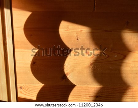 A photo of a wooden wall made of round logs illuminated by the sun, with sharp shadows