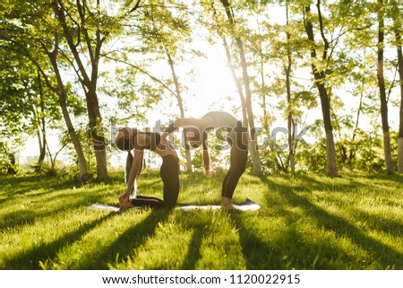 Photo of two ladies standing and  training yoga poses together outdoors. Young women practicing yoga with beautiful view on background