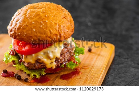 burger with meat, cheese and vegetables on wooden board