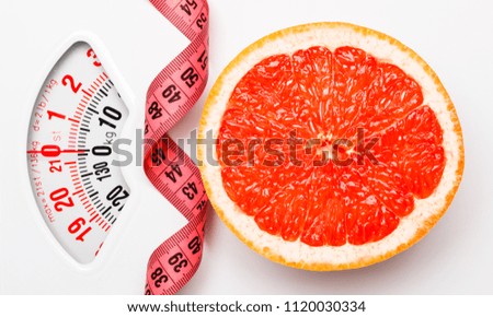 Dieting healthy eating slim down concept. Closeup grapefruit slice with measuring tape on white weight scale