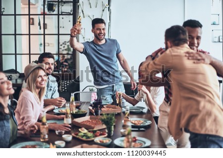 All you need is a birthday party! Handsome young man toasting and smiling while two men embracing 