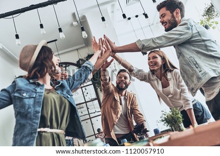Friends forever! Group of young people giving each other high-five in a symbol of unity and smiling while having a dinner party           