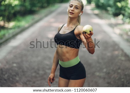 Young Sporty Woman in a Black Sportswear Holds Green Apple in the Openair. Concept of Healthy Lifestyle.