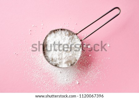 Measuring scoop with powder sugar on pink background, top view
