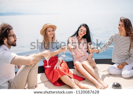 Horizontal portrait of young caucasian people toasting drinks on the yacht deck and laughing. Cheerful men and woman partying on a boat with amazing seaviews on background.