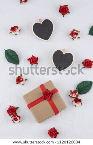 Brown gift box and tiny heart blackboard decorate with red rose paper flowers on white fabric