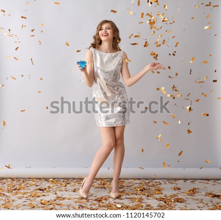 Beautiful young woman with drink and falling confetti on grey background
