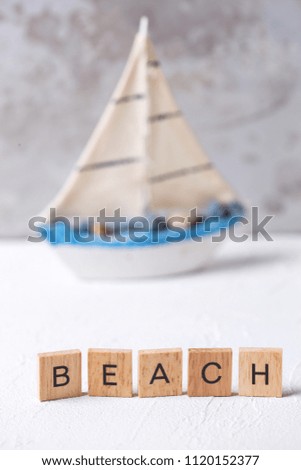 Word beach  from wooden blocks  and boat toy against grey wall. Selective focus.