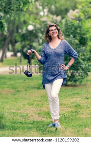 Adult happy pretty smiling Caucasian 50-years old woman standing and posing with photo camera at summer green park.