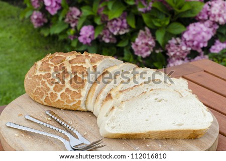 Tiger Bread - Crusty sliced white bread on a wooden board outdoors.