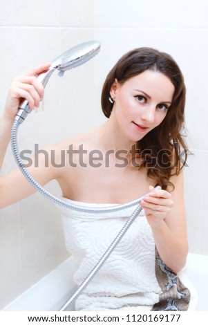 Beautiful young woman wraped in towel in bathroom after shower holds shower head
