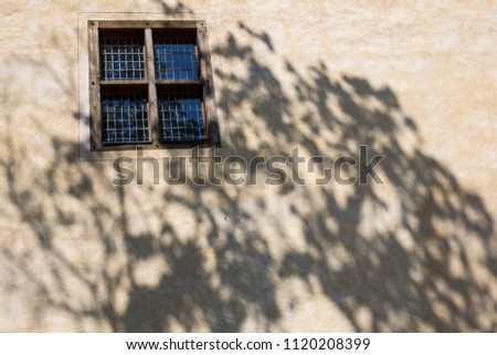 part of the wall of the old building, on it a shadow from a tree and a window with a lattice - prison