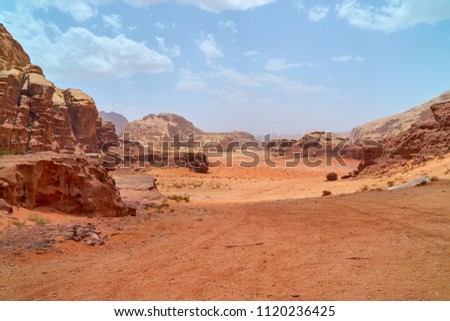 Wadi Rum desert, Jordan, The Valley of the Moon. Orange sand, haze, clouds. Designation as a UNESCO World Heritage Site. Red planet Mars  landscape. Offroad adventures travel background.               Royalty-Free Stock Photo #1120236425