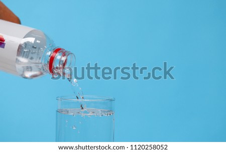 Pouring pure mineral water from plastic bottle into glass with blue background.