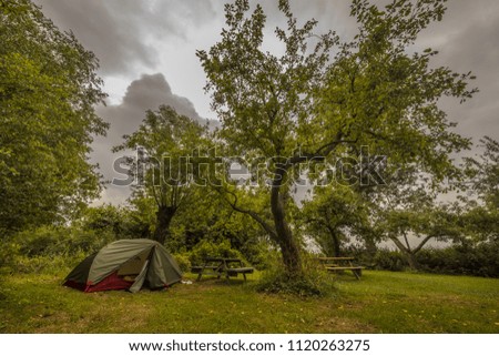 Small tent in orchard under cloudy sky. Well camouflaged and blending in environment
