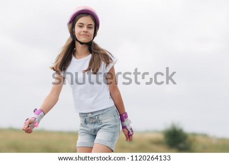 Close up portrait of little girl rinking outdoors. Girl has roller skates equipment, wearing pink helmet.