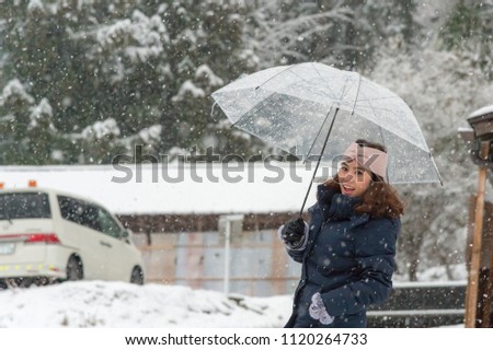 woman standing and holding transparent umbrella in the winter and snow is falling. she smile and happy, concept of travel, trip and holiday