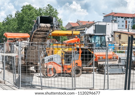 Industrial machinery for asphalt pavement work on the street construction and reconstruction site surrounded with metal safety fence