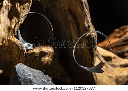 modern metal ear rings on root and black stone background with hard light effect