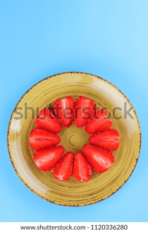 Strawberries on a blue background, halves of a red strawberry in the form of a circle, red berries on a yellow plate, vegetarian food for breakfast, copy space, blank for a designer, creative