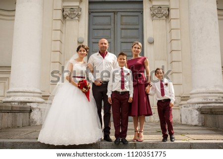 Perfect daughter bride with parents and younger brother posing at camera while taking a picture at the wedding day. Standing near the ancient building.