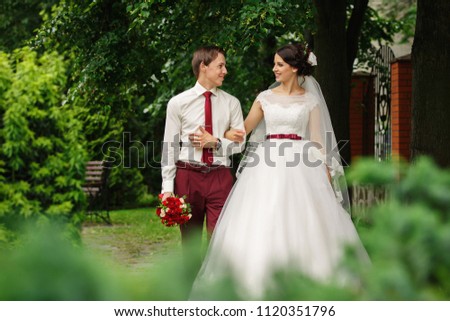 Elegant groom and stunning bride in incredible dress walking together after wedding ceremony. In the park. Happy marriage.