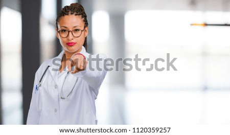 Portrait of a young black doctor woman cheerful and smiling pointing to the front