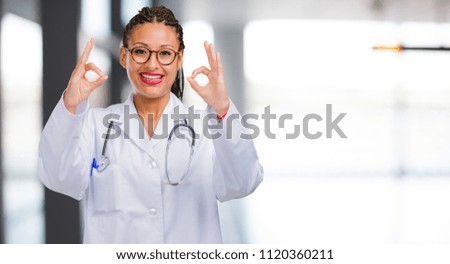 Portrait of a young black doctor woman cheerful and confident doing ok gesture, excited and screaming, concept of approval and success