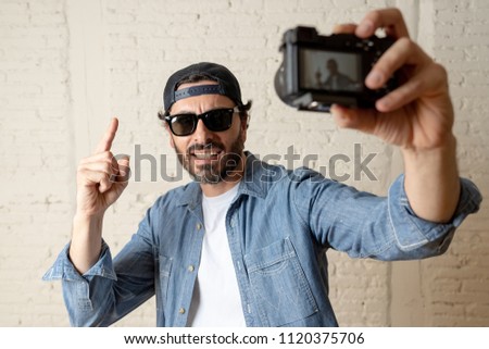young attractive man wearing casual clothes sunglasses in hipster style modern look holding photo camera shooting self portrait selfie picture or recording video in internet blog and blogger concept.