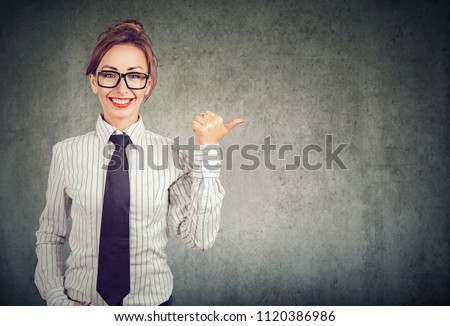 Cheerful businesswoman in tie pointing away with finger giving indication on gray background