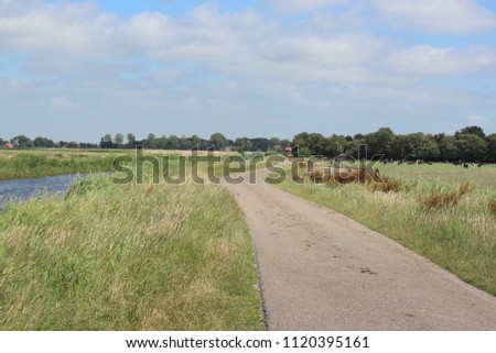 A beautiful small country road through meadows and a waterway.