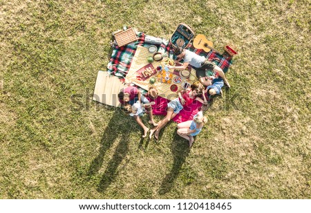 Aerial drone view of happy families having fun with kids at picnic barbecue party - Multiracial happiness and love concept with mixed race people playing with children at park - Warm bright filter Royalty-Free Stock Photo #1120418465