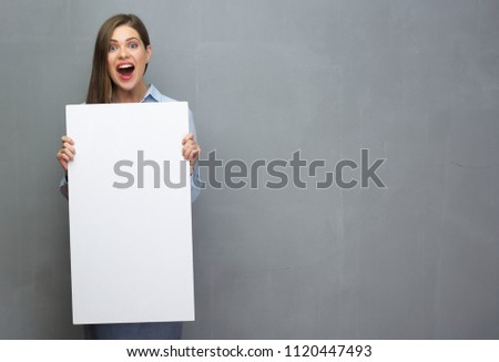 Sirprising woman with open mouth holding white blank board. Gray wall back.