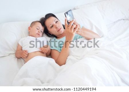 mom and baby lie together in bed and take selfies