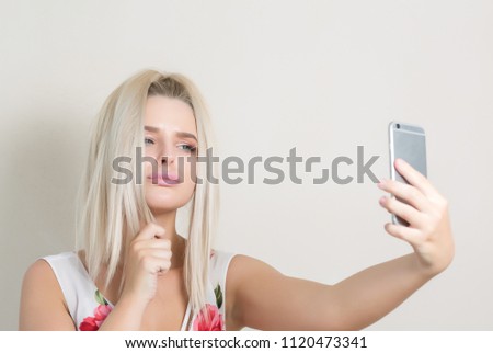 Cute blonde woman making self portrait on smartphone against a grey background