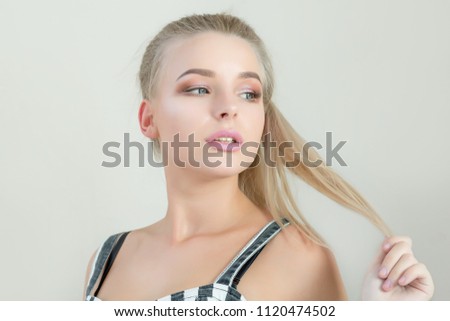Gorgeous blonde model pulling her hair, posing on a grey background